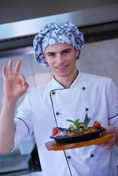 Handsome chef dressed in white uniform decorating pasta salad and seafood fish in modern kitchen