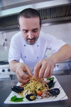 Handsome chef dressed in white uniform decorating pasta salad and seafood fish in modern kitchen