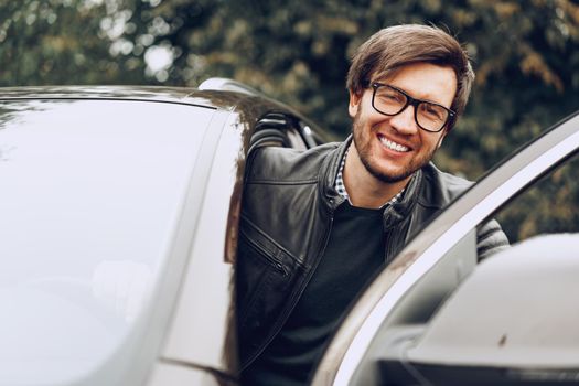 Stylish man in glasses sits in a car, close up portrait