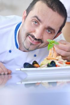 Handsome chef dressed in white uniform decorating pasta salad and seafood fish in modern kitchen