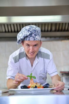 Handsome chef dressed in white uniform decorating pasta salad and seafood fish in modern kitchen