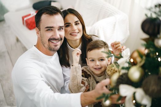 Family of 3 decorating a Christmas tree at home, close up