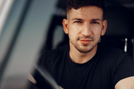 Handsome young man driver looking through the window of his off-road car, close up portrait