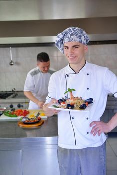 Handsome chef dressed in white uniform decorating pasta salad and seafood fish in modern kitchen