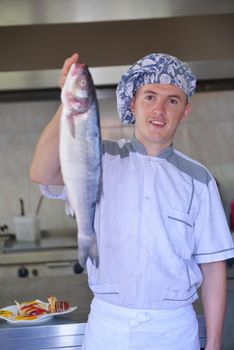 Handsome chef dressed in white uniform decorating pasta salad and seafood fish in modern kitchen