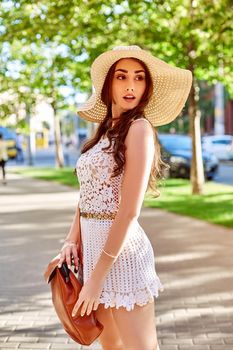 Sunny lifestyle fashion portrait of young stylish hipster woman walking on the street, wearing trendy outfit, straw hat, travel with backpack. Street style