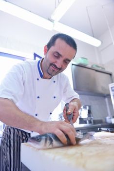 Handsome chef dressed in white uniform decorating pasta salad and seafood fish in modern kitchen