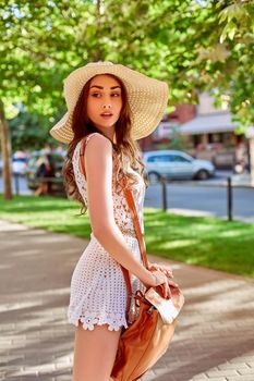 Sunny lifestyle fashion portrait of young stylish hipster woman walking on the street, wearing trendy outfit, straw hat, travel with backpack. Street style