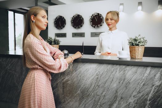 Blonde woman hotel guest checking-in at front desk in hotel close up