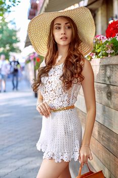 Sunny lifestyle fashion portrait of young stylish woman walking on the street, wearing trendy outfit, straw hat, travel with backpack.