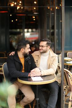 Two cacuasian gays talking at street cafe and holding hands. Concept of same sex couple and lgbt.