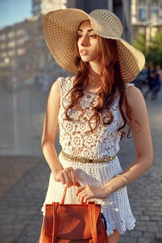 Close up portrait of a beautiful young woman near shop window during a sunny day. Lifestyle outdoors. Sunny lifestyle fashion portrait of young stylish woman walking on the street, wearing trendy outfit, straw hat, travel with backpack.