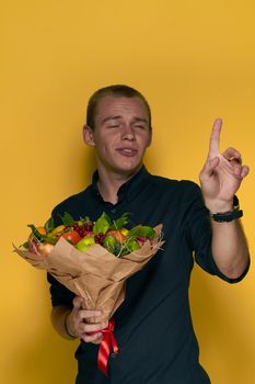 man with a bouquet of fruits in a black shirt yellow background. High quality photo