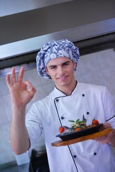 Handsome chef dressed in white uniform decorating pasta salad and seafood fish in modern kitchen