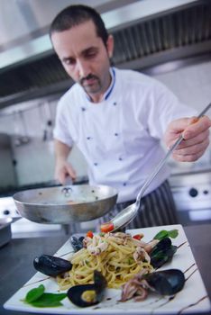 Handsome chef dressed in white uniform decorating pasta salad and seafood fish in modern kitchen