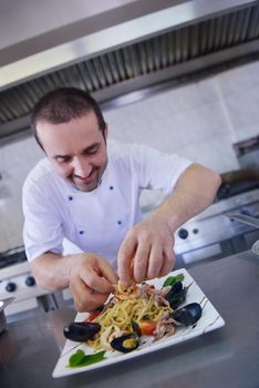 Handsome chef dressed in white uniform decorating pasta salad and seafood fish in modern kitchen