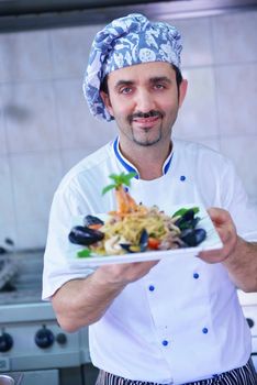 Handsome chef dressed in white uniform decorating pasta salad and seafood fish in modern kitchen