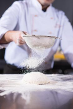 chef sprinkling flour over fresh pizza dough on kitchen table