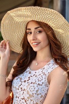 Sunny lifestyle fashion portrait of young pretty trendy girl posing at the city in Europe, summer street fashion, straw hat, laughing and smiling portrait.