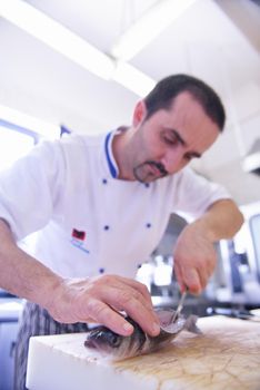 Handsome chef dressed in white uniform decorating pasta salad and seafood fish in modern kitchen