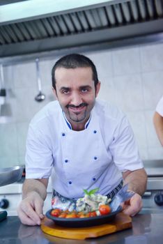 Handsome chef dressed in white uniform decorating pasta salad and seafood fish in modern kitchen