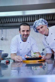 Handsome chef dressed in white uniform decorating pasta salad and seafood fish in modern kitchen