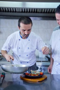 Handsome chef dressed in white uniform decorating pasta salad and seafood fish in modern kitchen