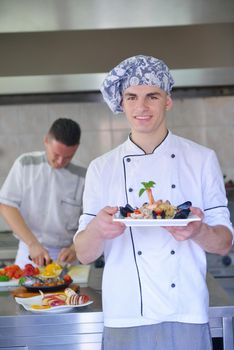 Handsome chef dressed in white uniform decorating pasta salad and seafood fish in modern kitchen