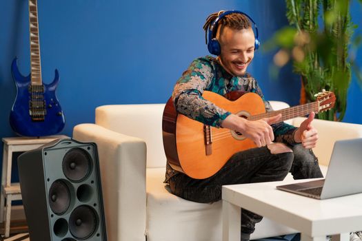 Young man sitting in his room and watching guitar tutorial on laptop close up