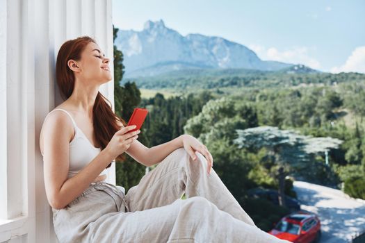 Attractive young woman sitting on the balcony with phone beautiful mountain view summer Mountain View. High quality photo