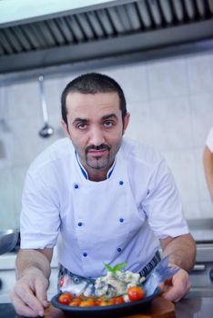 Handsome chef dressed in white uniform decorating pasta salad and seafood fish in modern kitchen