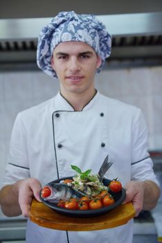 Handsome chef dressed in white uniform decorating pasta salad and seafood fish in modern kitchen