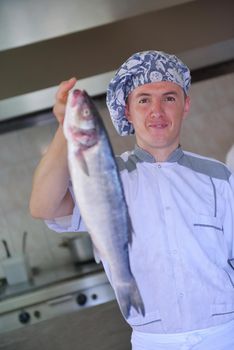 Handsome chef dressed in white uniform decorating pasta salad and seafood fish in modern kitchen