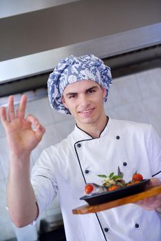 Handsome chef dressed in white uniform decorating pasta salad and seafood fish in modern kitchen