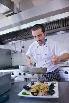 Handsome chef dressed in white uniform decorating pasta salad and seafood fish in modern kitchen