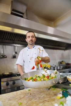 Handsome chef dressed in white uniform decorating pasta salad and seafood fish in modern kitchen