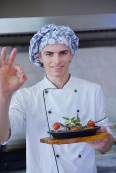 Handsome chef dressed in white uniform decorating pasta salad and seafood fish in modern kitchen