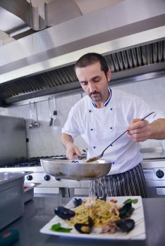 Handsome chef dressed in white uniform decorating pasta salad and seafood fish in modern kitchen