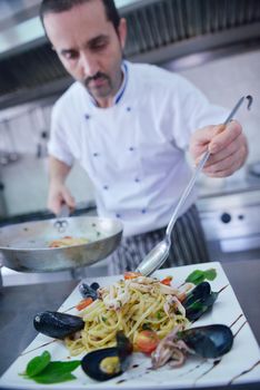 Handsome chef dressed in white uniform decorating pasta salad and seafood fish in modern kitchen