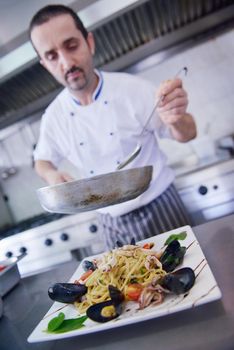 Handsome chef dressed in white uniform decorating pasta salad and seafood fish in modern kitchen