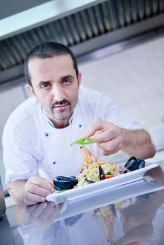 Handsome chef dressed in white uniform decorating pasta salad and seafood fish in modern kitchen