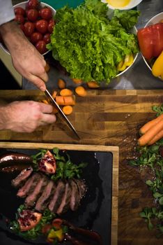 top view of Chef hands in hotel or restaurant kitchen serving beef steak with vegetable decoration