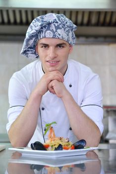 Handsome chef dressed in white uniform decorating pasta salad and seafood fish in modern kitchen