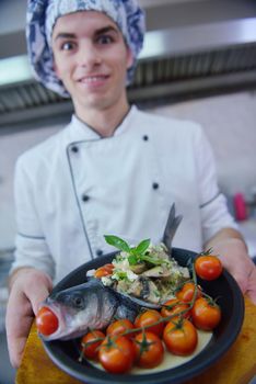 Handsome chef dressed in white uniform decorating pasta salad and seafood fish in modern kitchen