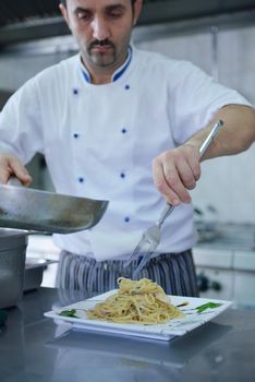 Handsome chef dressed in white uniform decorating pasta salad and seafood fish in modern kitchen