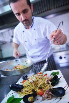 Handsome chef dressed in white uniform decorating pasta salad and seafood fish in modern kitchen