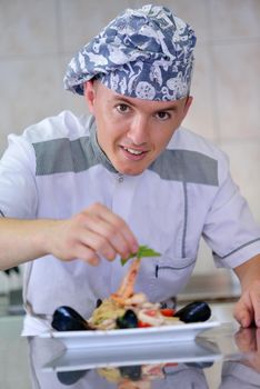 Handsome chef dressed in white uniform decorating pasta salad and seafood fish in modern kitchen