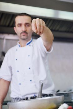 Handsome chef dressed in white uniform decorating pasta salad and seafood fish in modern kitchen