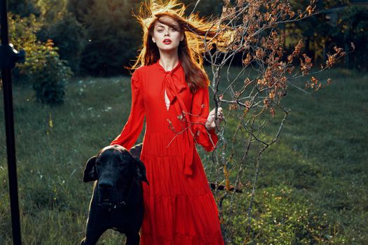 beautiful woman in a red dress outdoors with a black dog friendship. High quality photo