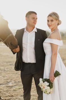 Bride and groom posing with a horse on sunset close up